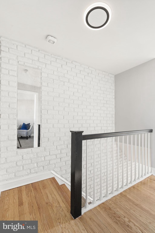 hall with wood-type flooring and brick wall