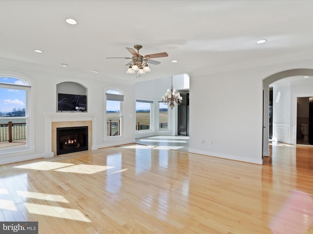 unfurnished living room with crown molding, a healthy amount of sunlight, ceiling fan with notable chandelier, and light hardwood / wood-style floors