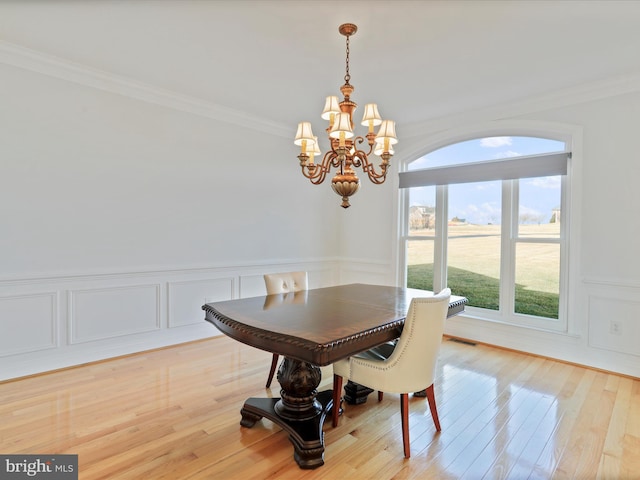 dining area with ornamental molding, an inviting chandelier, and light wood-type flooring