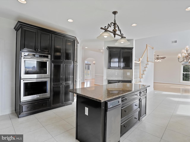 kitchen featuring dark stone countertops, a center island, light tile patterned flooring, decorative backsplash, and stainless steel double oven