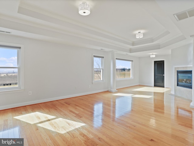 empty room with a raised ceiling, ornamental molding, light wood-type flooring, and a tile fireplace