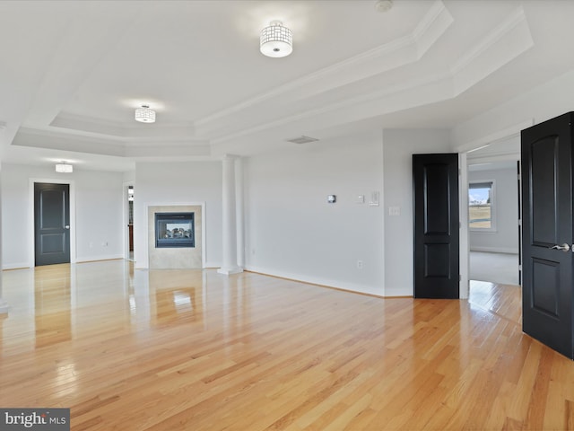 unfurnished living room with crown molding, a tray ceiling, and light hardwood / wood-style flooring