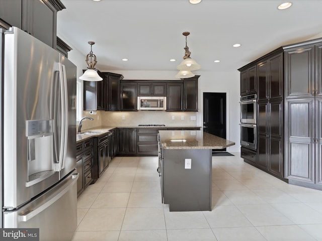 kitchen with sink, appliances with stainless steel finishes, a center island, light stone counters, and decorative light fixtures