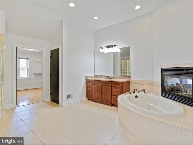 bathroom featuring tile patterned flooring, vanity, tiled bath, and a tile fireplace