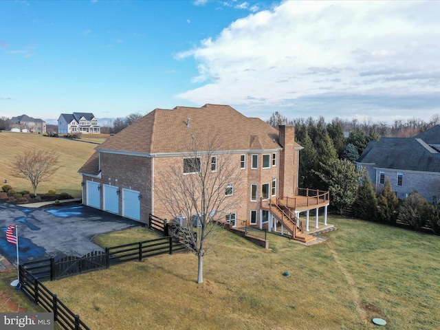 rear view of property with a garage, a wooden deck, and a lawn