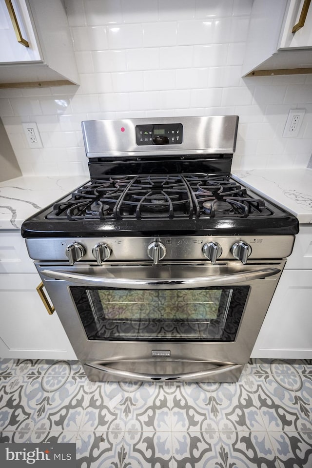 details with tasteful backsplash, stainless steel range with gas cooktop, white cabinets, and light stone counters