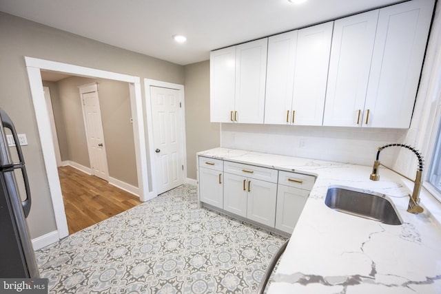 kitchen featuring sink, stainless steel fridge, white cabinets, backsplash, and light stone countertops