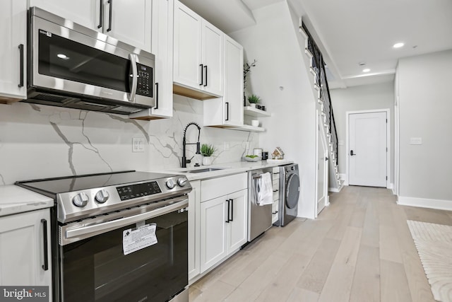 kitchen featuring washer / dryer, sink, light stone counters, appliances with stainless steel finishes, and white cabinets