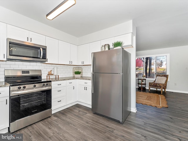 kitchen with white cabinetry, appliances with stainless steel finishes, backsplash, and dark stone countertops