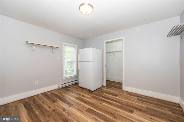 unfurnished bedroom featuring a closet, baseboards, freestanding refrigerator, wood finished floors, and a baseboard radiator