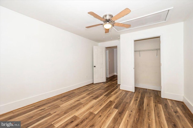 unfurnished bedroom with wood finished floors, a closet, attic access, baseboards, and a ceiling fan