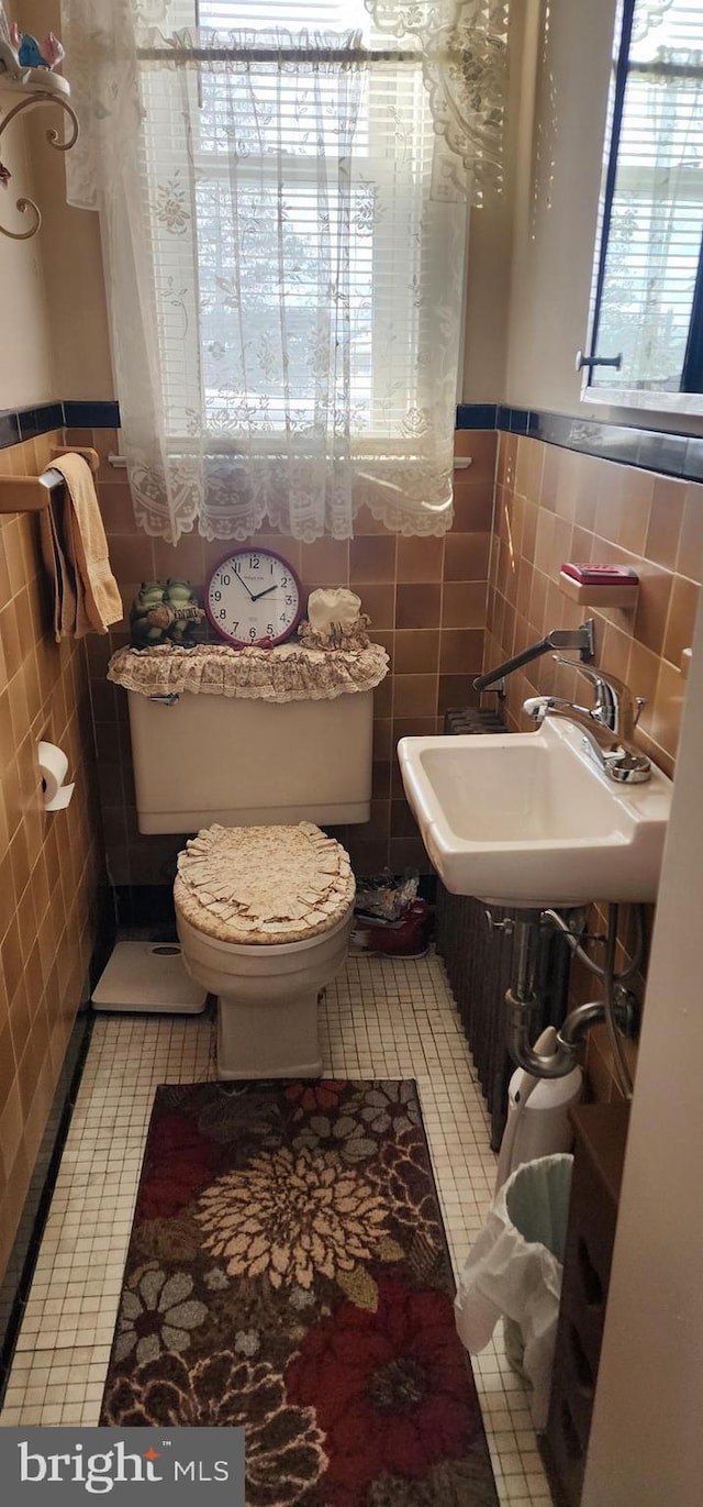 bathroom featuring tile patterned floors, toilet, sink, and tile walls