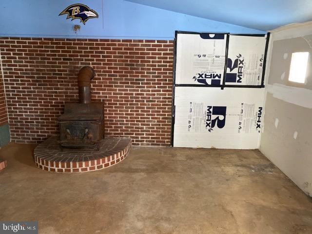 unfurnished living room featuring lofted ceiling, a wood stove, and concrete floors