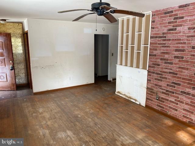 unfurnished room with dark hardwood / wood-style floors, ceiling fan, and brick wall