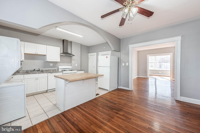 kitchen featuring wall chimney range hood, white appliances, wooden counters, a center island, and white cabinets