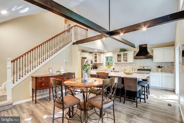 dining space featuring beamed ceiling, high vaulted ceiling, and light hardwood / wood-style floors