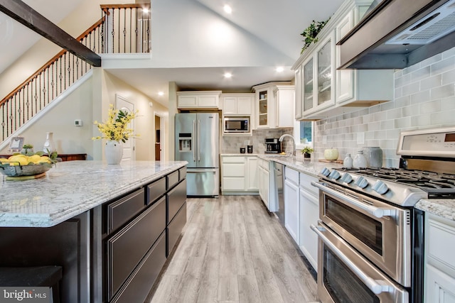 kitchen featuring white cabinetry, custom exhaust hood, light stone counters, stainless steel appliances, and light hardwood / wood-style flooring