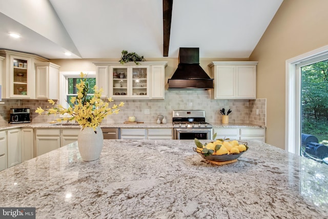 kitchen featuring lofted ceiling, stainless steel gas range oven, light stone countertops, and premium range hood