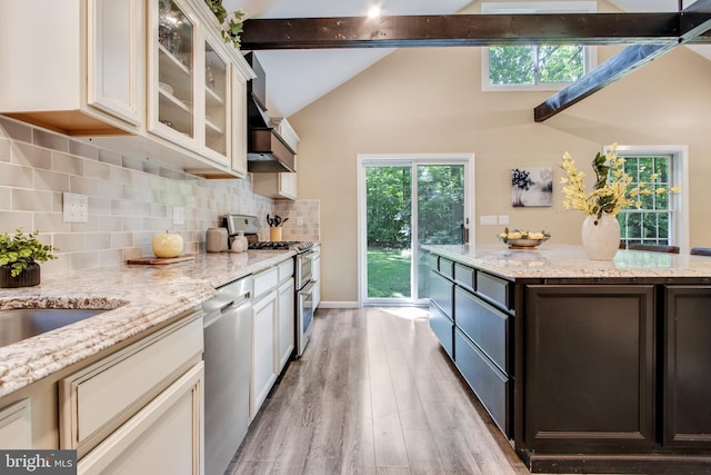 kitchen with appliances with stainless steel finishes, lofted ceiling with beams, tasteful backsplash, dark brown cabinetry, and light stone countertops