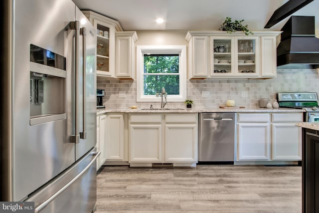 kitchen featuring sink, premium range hood, appliances with stainless steel finishes, light stone counters, and light wood-type flooring