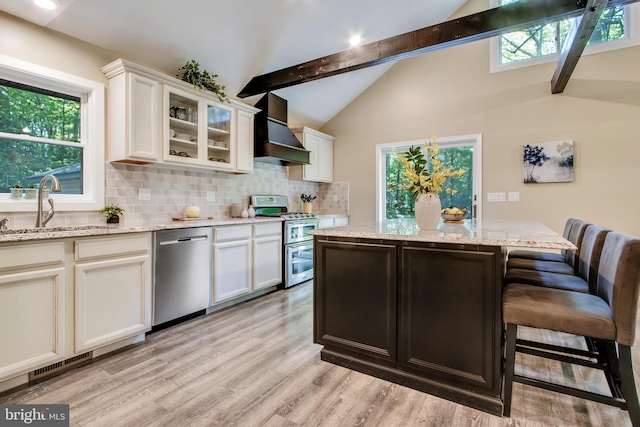 kitchen with sink, white cabinetry, stainless steel appliances, light stone countertops, and wall chimney range hood