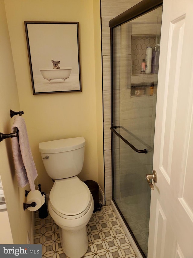 bathroom featuring a shower with door and toilet