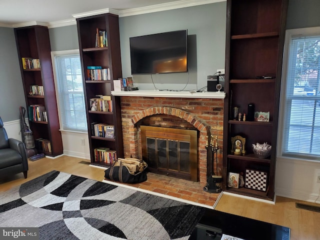 living room featuring built in features, a fireplace, ornamental molding, and light hardwood / wood-style floors