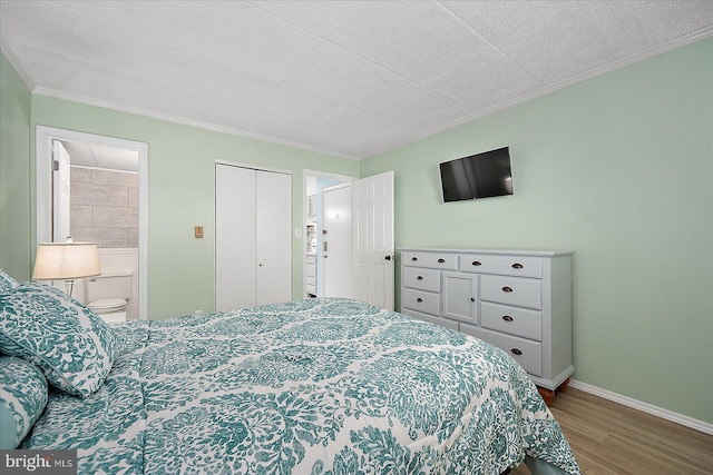 bedroom featuring hardwood / wood-style flooring, ornamental molding, ensuite bath, and a closet