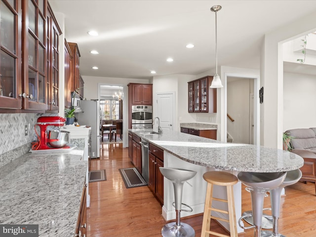 kitchen featuring backsplash, hanging light fixtures, light hardwood / wood-style floors, light stone counters, and stainless steel appliances