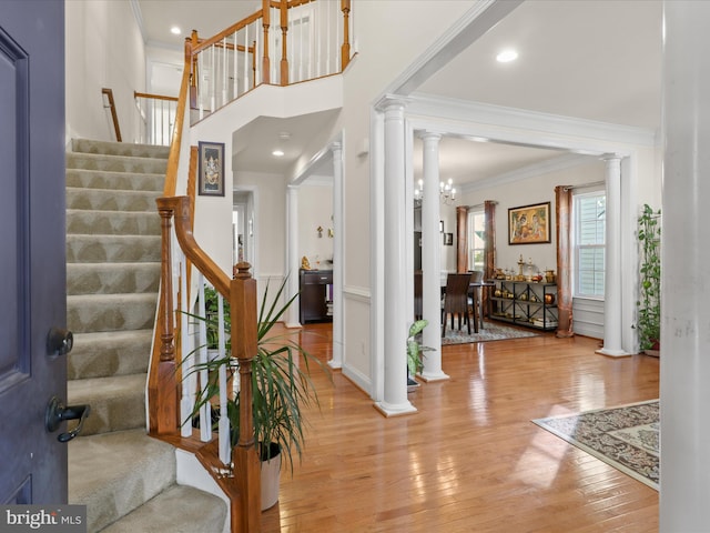 entrance foyer with decorative columns, crown molding, a high ceiling, and light hardwood / wood-style flooring