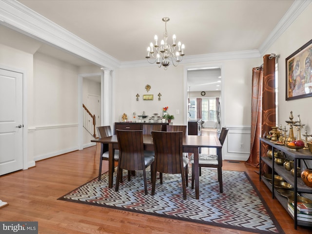 dining area featuring hardwood / wood-style floors, crown molding, a notable chandelier, and ornate columns