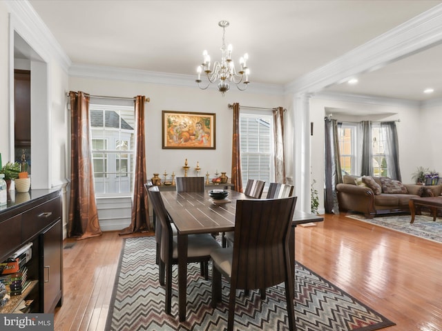 dining room featuring hardwood / wood-style flooring, ornamental molding, decorative columns, and an inviting chandelier