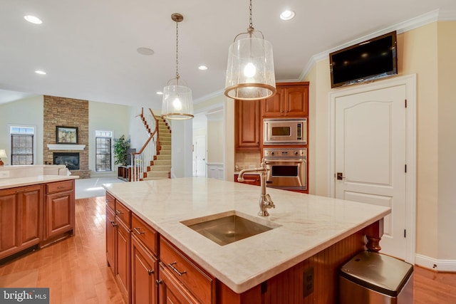 kitchen with appliances with stainless steel finishes, decorative light fixtures, an island with sink, sink, and light wood-type flooring