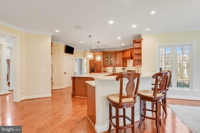 kitchen featuring a kitchen bar, kitchen peninsula, decorative columns, and custom range hood