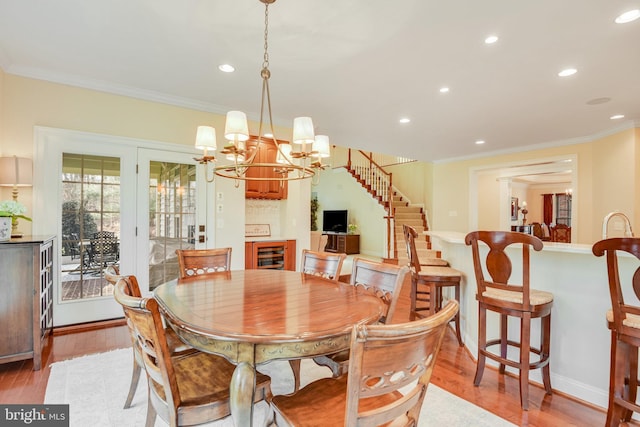 dining area with ornate columns, ornamental molding, beverage cooler, and light hardwood / wood-style flooring