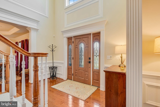 entryway with hardwood / wood-style floors, ornamental molding, decorative columns, and a high ceiling