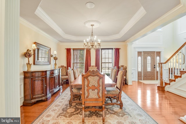 dining space featuring a raised ceiling, crown molding, a notable chandelier, and light hardwood / wood-style flooring