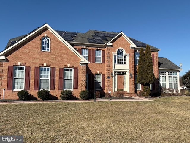 view of front facade featuring a front yard, solar panels, and brick siding