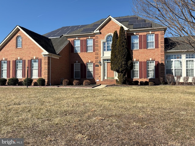 view of front of home with brick siding, a front lawn, and roof mounted solar panels