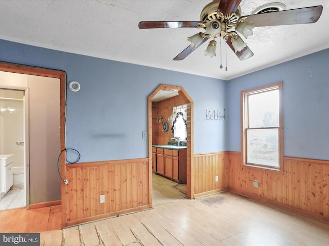 spare room with sink, light hardwood / wood-style floors, ceiling fan, and wood walls