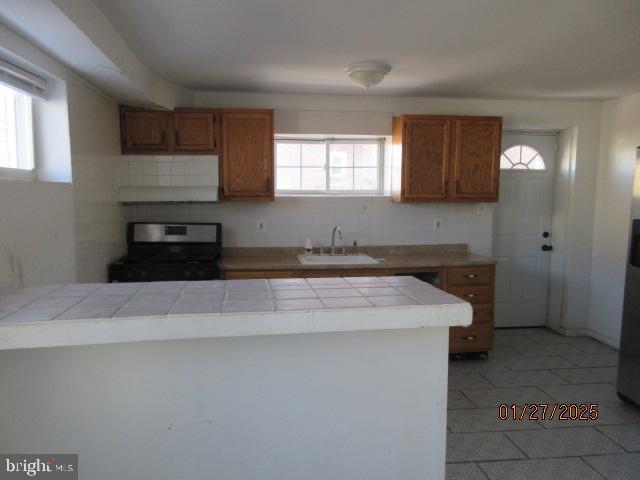 kitchen featuring sink, tile countertops, decorative backsplash, and stainless steel electric range