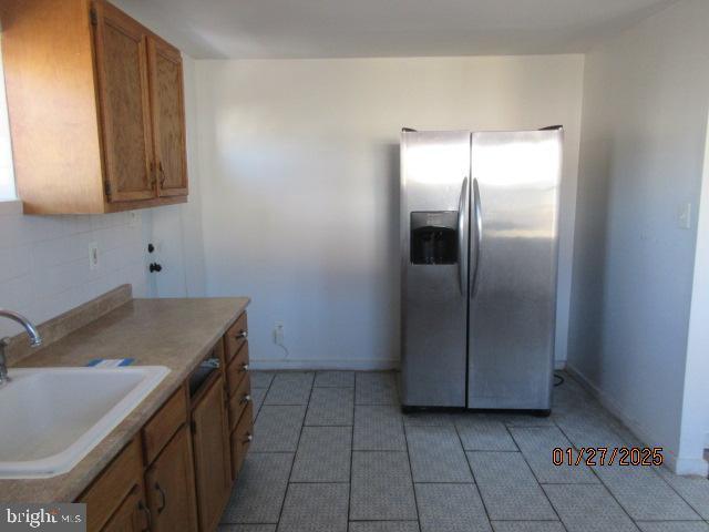 kitchen featuring stainless steel refrigerator with ice dispenser, sink, light tile patterned flooring, and backsplash