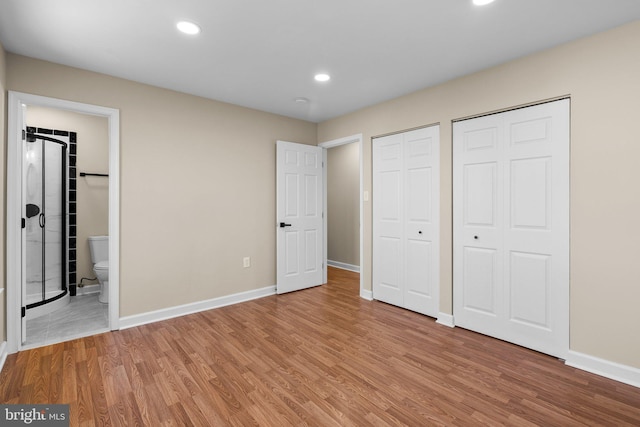 unfurnished bedroom with multiple closets, wood-type flooring, and ensuite bath