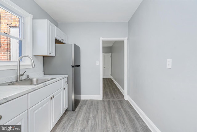 kitchen with white cabinetry, sink, light hardwood / wood-style floors, and stainless steel refrigerator