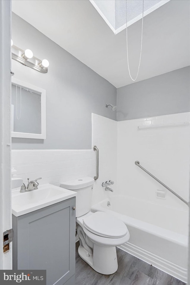 full bathroom featuring hardwood / wood-style flooring, tile walls, vanity, shower / washtub combination, and toilet