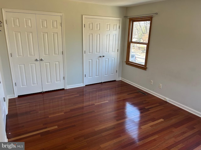 unfurnished bedroom with two closets and dark wood-type flooring