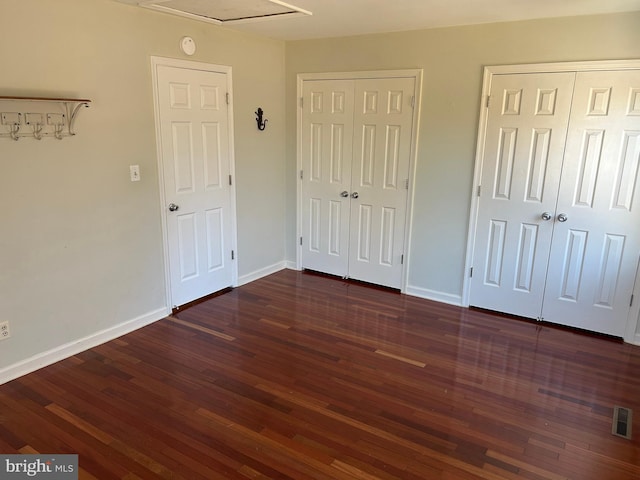 unfurnished bedroom featuring dark hardwood / wood-style flooring and two closets