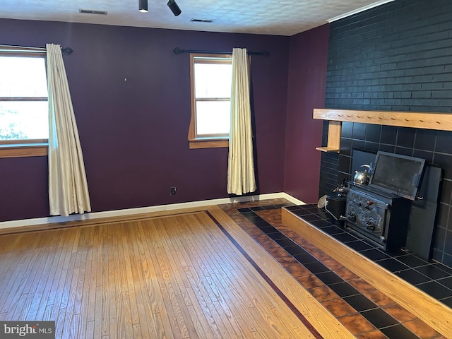 unfurnished living room with wood-type flooring, a textured ceiling, and a wood stove