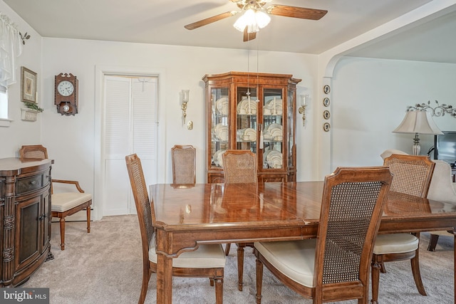 dining room with light carpet, ceiling fan, and arched walkways