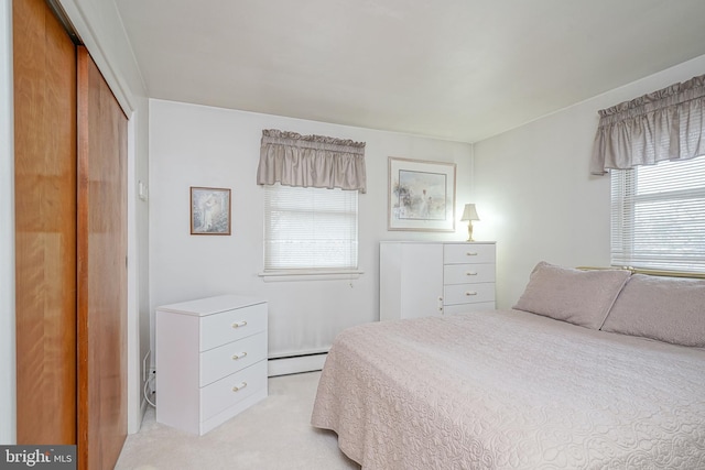 bedroom with a baseboard heating unit, a closet, and light carpet